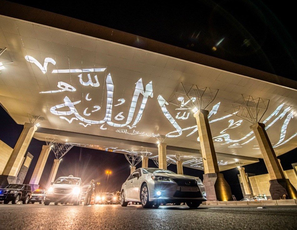 سقف بوابة المدينة المنورة المزخرف مضاءً ليلًا والسيارات تعبر تحته